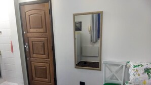 A room with a wooden door, a mirror with a decorative frame, a green chair, and a bed with floral bedding. - Charming studio 5 mins walk from Copacabana beach (Copacabana)