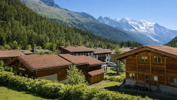 Un pueblo de montaña con casas de madera, cielo despejado y picos nevados al fondo.