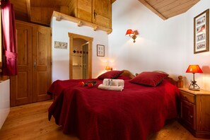 Un dormitorio con estructura de madera, cubre cama rojo, dos lámparas de noche y un armario de madera.