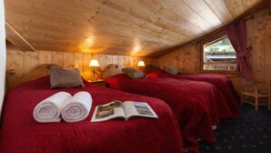 Habitación de cabaña de madera con dos camas, cada una con colcha y almohadas rojas, una ventana con cortinas y una silla.