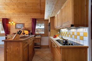 Interior de una cabaña de madera con una cocina que incluye armarios de madera, salpicadero de azulejos y ventana con vistas a un paisaje nevado.