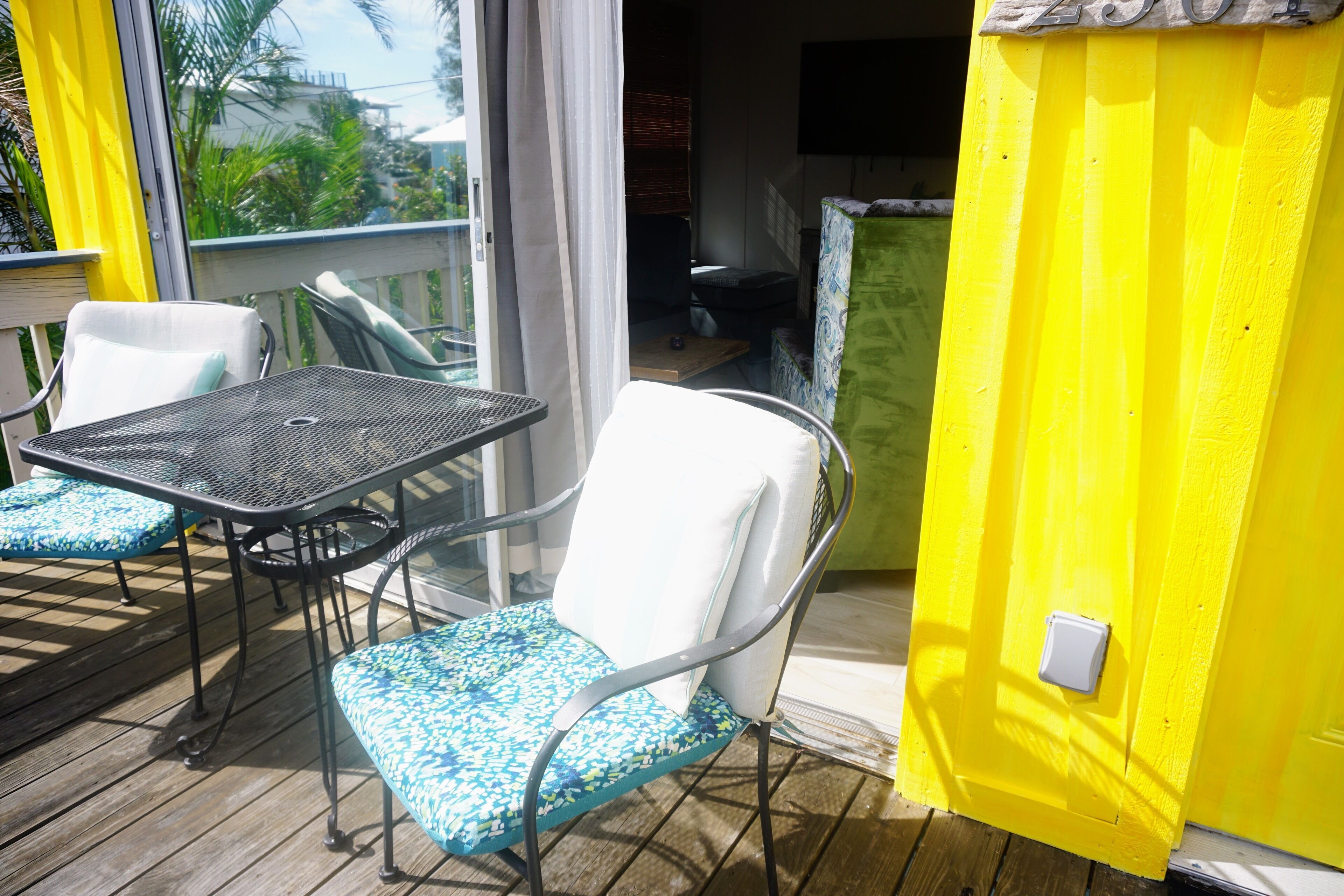 Un balcon avec une table et des chaises, une porte-fenêtre coulissante et un mur jaune.