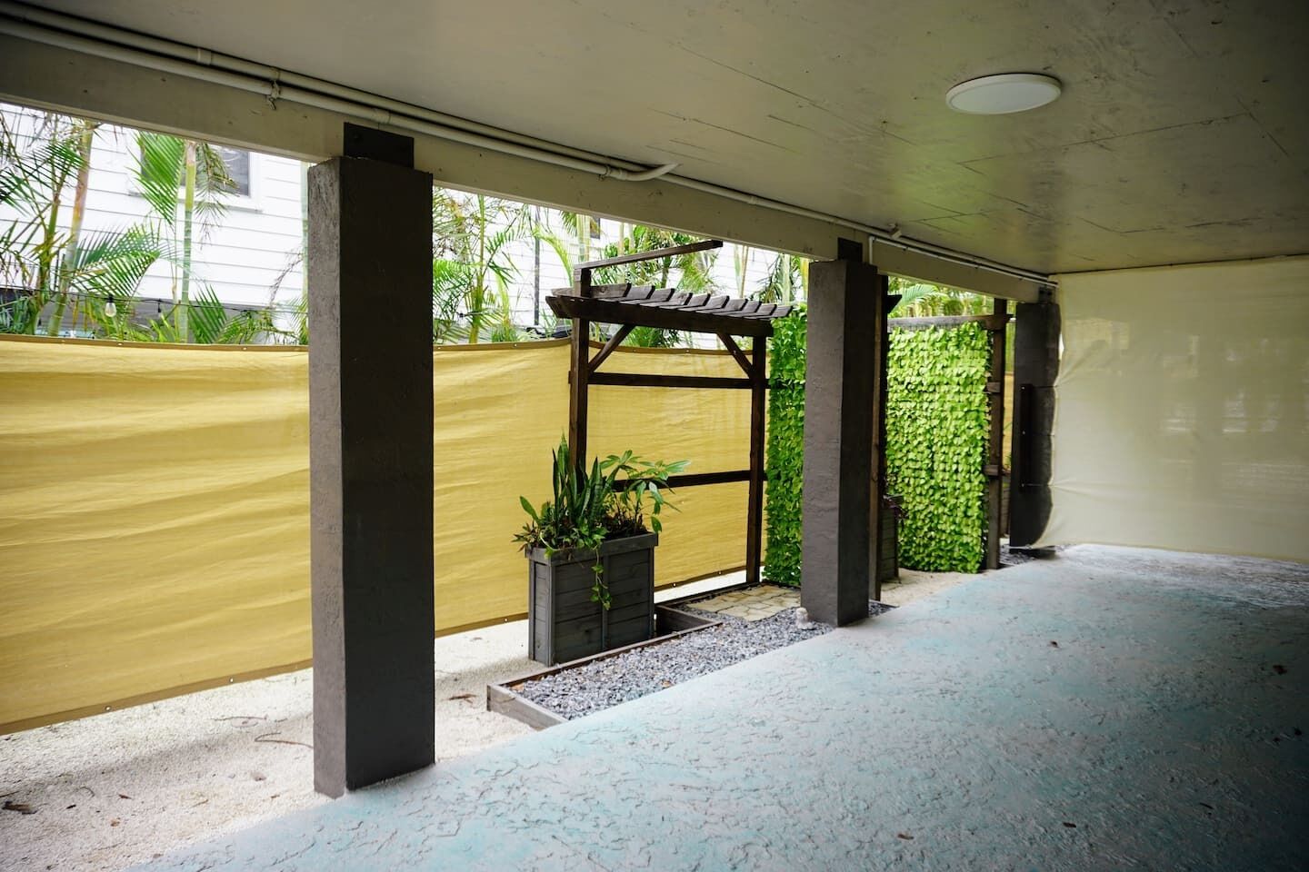 Un espace extérieur abrité doté d’un sol en béton, d’une clôture jaune et d’une structure de pergola en bois.