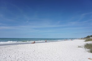 Een breed zandstrand met een heldere blauwe lucht en een rustige zee.