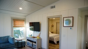 A room with a blue sofa, a TV, a desk with drawers, a bed with a patterned bedspread, and a framed picture on the wall. - Fall Specials Available! Pet Friendly! Steps to white sandy beaches and the bay!  Automatic discounts applied for stays longer than 7 days and 30 days! (Bradenton Beach)