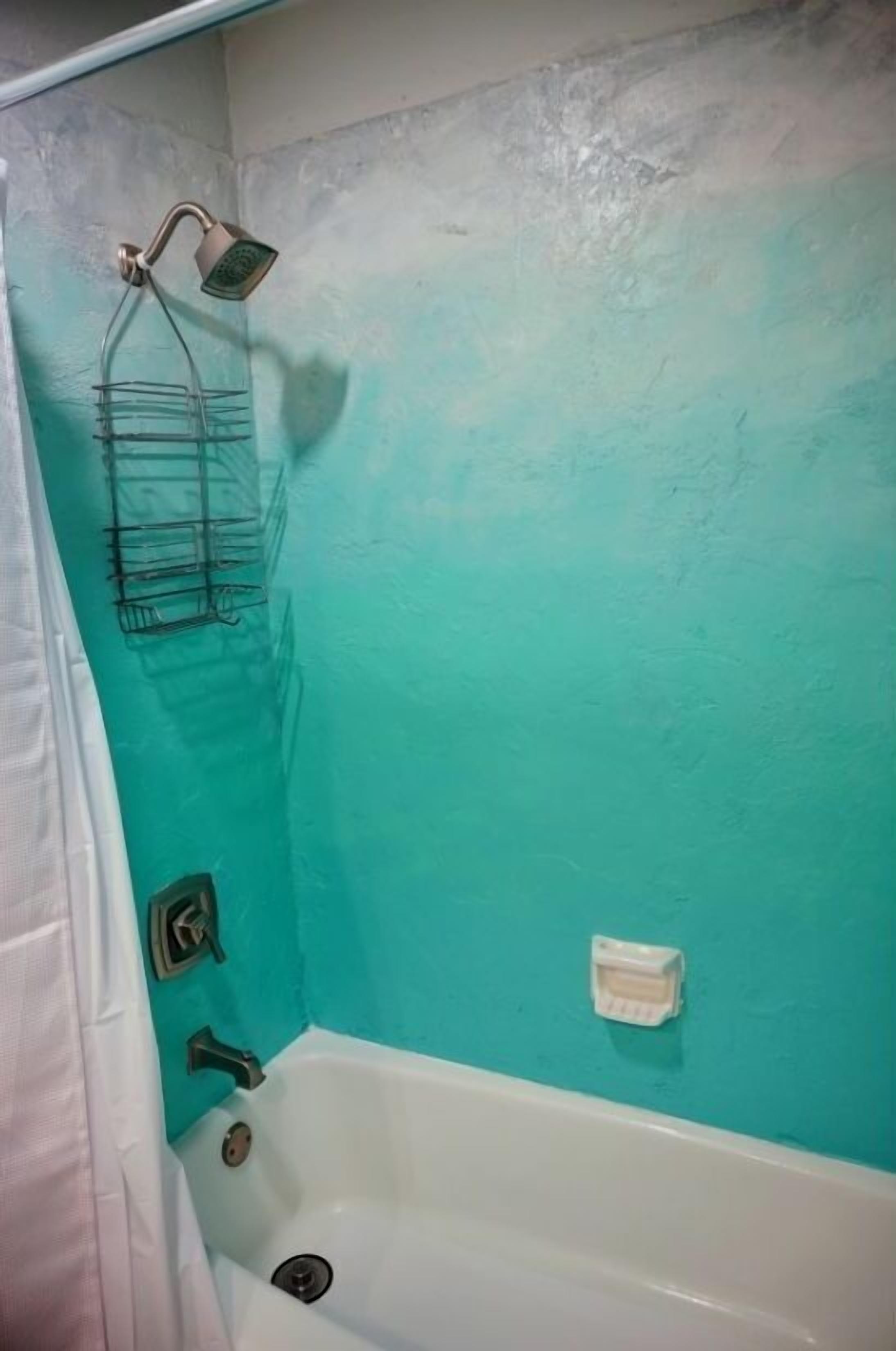 Een badkamer met een turquoise wand, een witte badkuip, een douchekop en een zeepbakje.