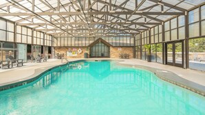 Una piscina interior con techo de cristal, zonas de estar y una pared de ladrillo con un flotador.