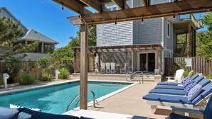 Un patio trasero con piscina, sillas de descanso y un pérgola de madera.