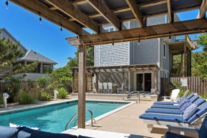 A backyard with a swimming pool, lounge chairs, and a wooden pergola.