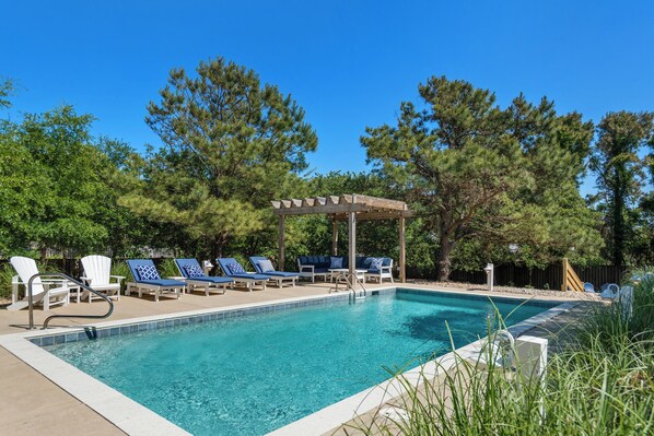 A swimming pool with lounge chairs and a pergola, surrounded by trees.