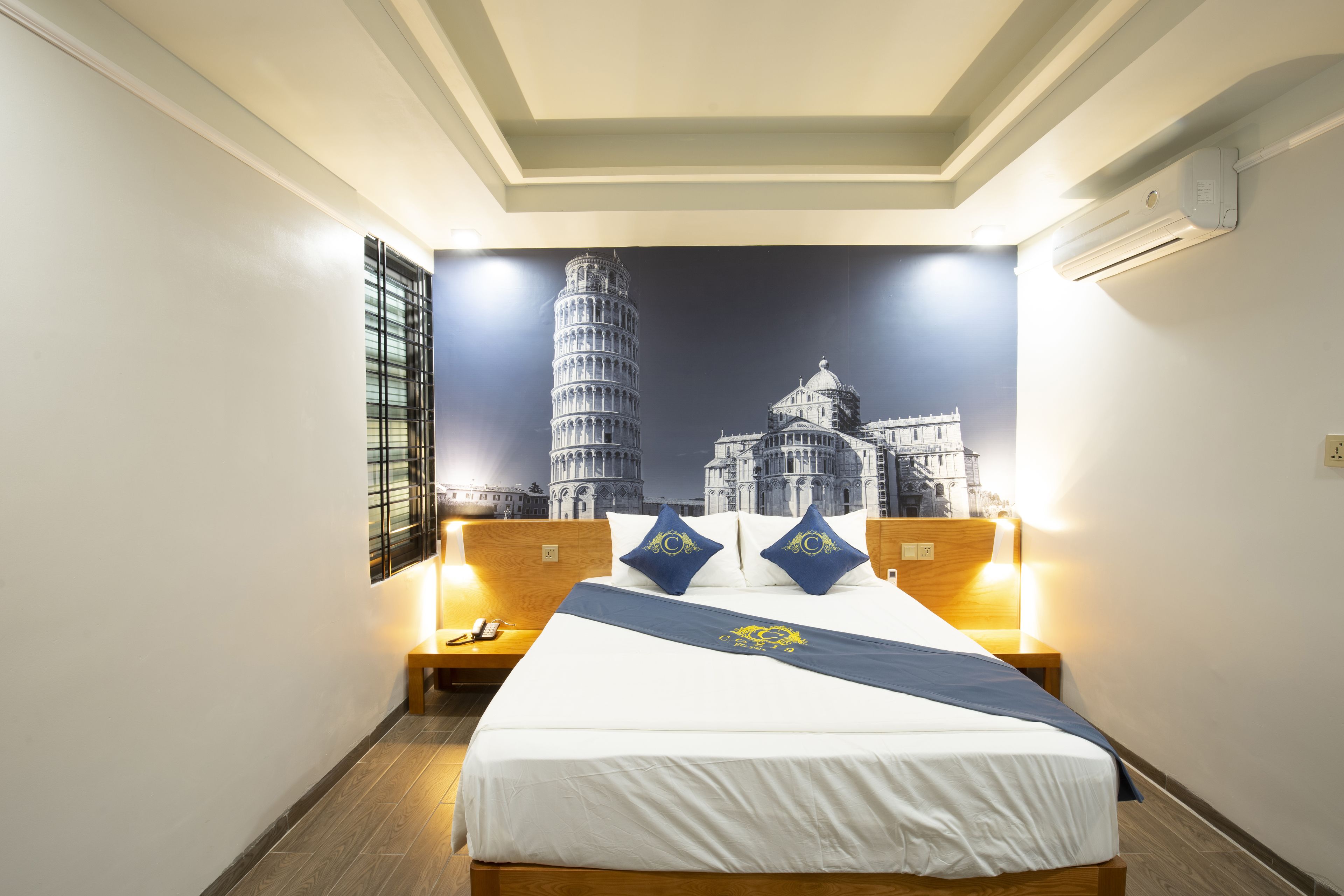 A hotel room with a bed, nightstands, and a wall mural of the Leaning Tower of Pisa.