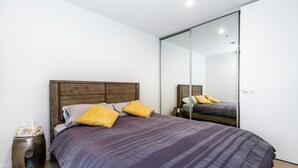 Une chambre à coucher moderne avec un grand lit, une tête de lit en bois et un miroir sur le mur.