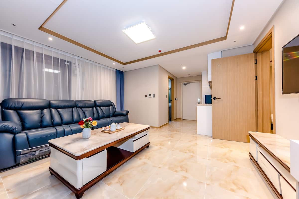 Un salón moderno con un sofá de cuero negro, una mesa de centro de madera y un suelo de mármol.
