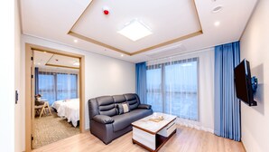 A modern hotel room with a black leather sofa, a wooden coffee table, and a TV mounted on the wall. - Hotel DK (Seogwipo)