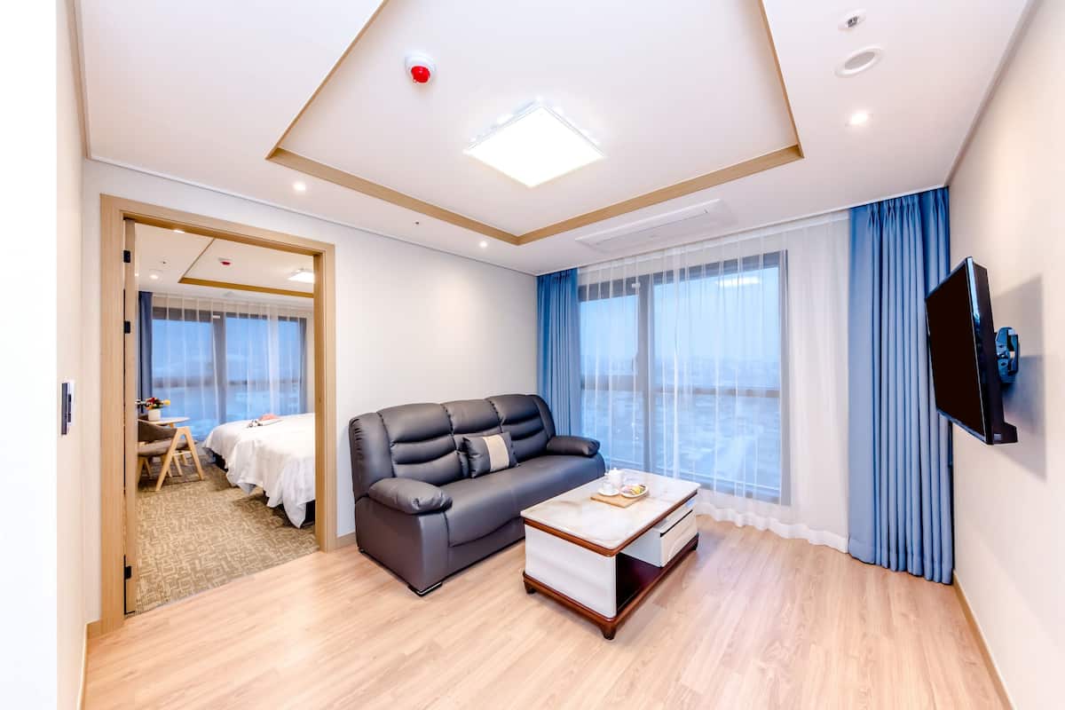 Una habitación de hotel moderna con un sofá de cuero negro, una mesa de centro de madera y un televisor montado en la pared.