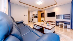A modern living room with a blue sofa, a coffee table, and a TV. - Hotel DK (Seogwipo)