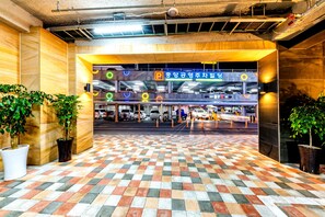 A parking garage entrance with a checkered floor pattern, multiple parking levels, and potted plants. - Hotel DK (Seogwipo)