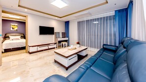 A modern hotel room with a large bed, a sofa, a TV, and a dining area. - Hotel DK (Seogwipo)