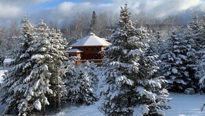 A wooden cabin surrounded by snow-covered trees. - Unique 'yurt' home in Bretton Woods  with hot tub, firepit, trails, beach, swimming, volleyball! (Bretton Woods)