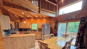 A wooden cabin interior with a kitchen, dining area, and large windows. - Unique 'yurt' home in Bretton Woods  with hot tub, firepit, trails, beach, swimming, volleyball! (Bretton Woods)
