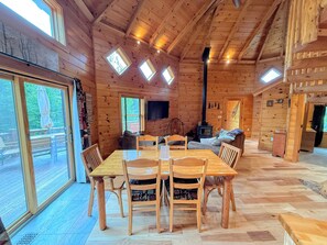A wooden cabin interior with a dining table, chairs, a sofa, a fireplace, and skylights.