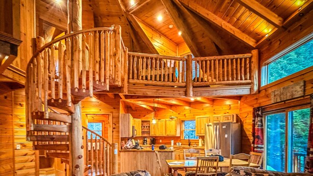 A log cabin interior with a wooden staircase, a dining area, and a living room with two sofas. - Unique 'yurt' home in Bretton Woods  with hot tub, firepit, trails, beach, swimming, volleyball! (Bretton Woods)