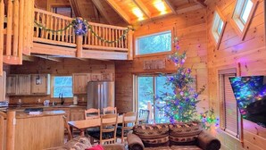 A cozy cabin interior with a wooden staircase, a dining area, a living room with a couch, a Christmas tree, and a television. - Unique 'yurt' home in Bretton Woods  with hot tub, firepit, trails, beach, swimming, volleyball! (Bretton Woods)