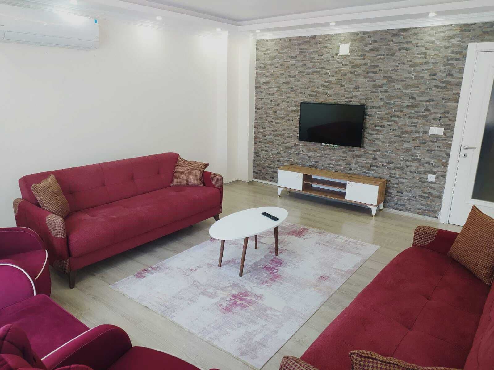 A living room with a red sofa, a white coffee table, and a stone-patterned wall.