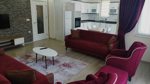 A modern living room with a red sofa, a small white table, and a kitchen area with white cabinets and a microwave. - Kaya House Daily Flat (Ortaca)