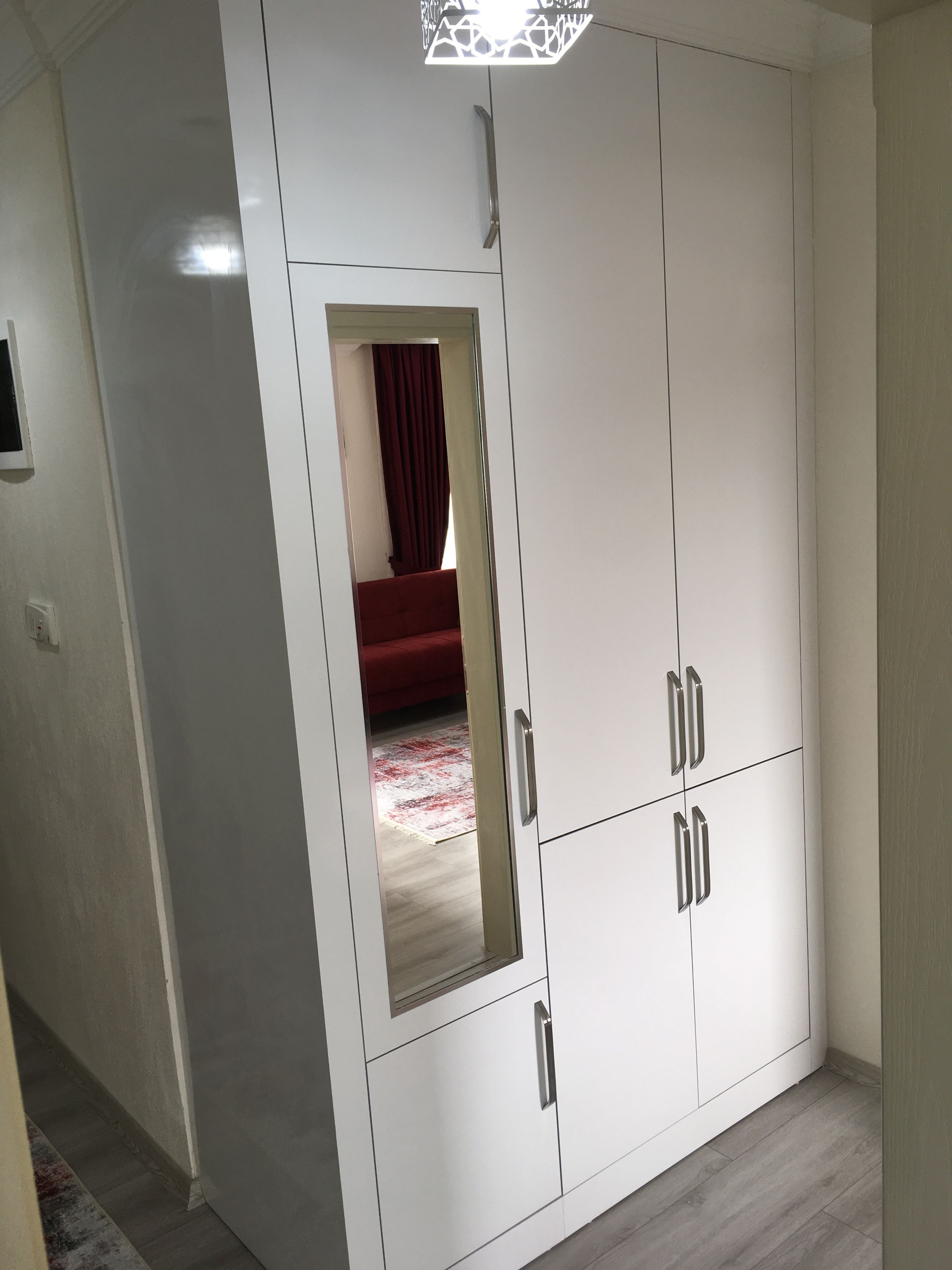 Um guarda-roupa branco com espelho, uma cama vermelha e um tapete estampado ao fundo.