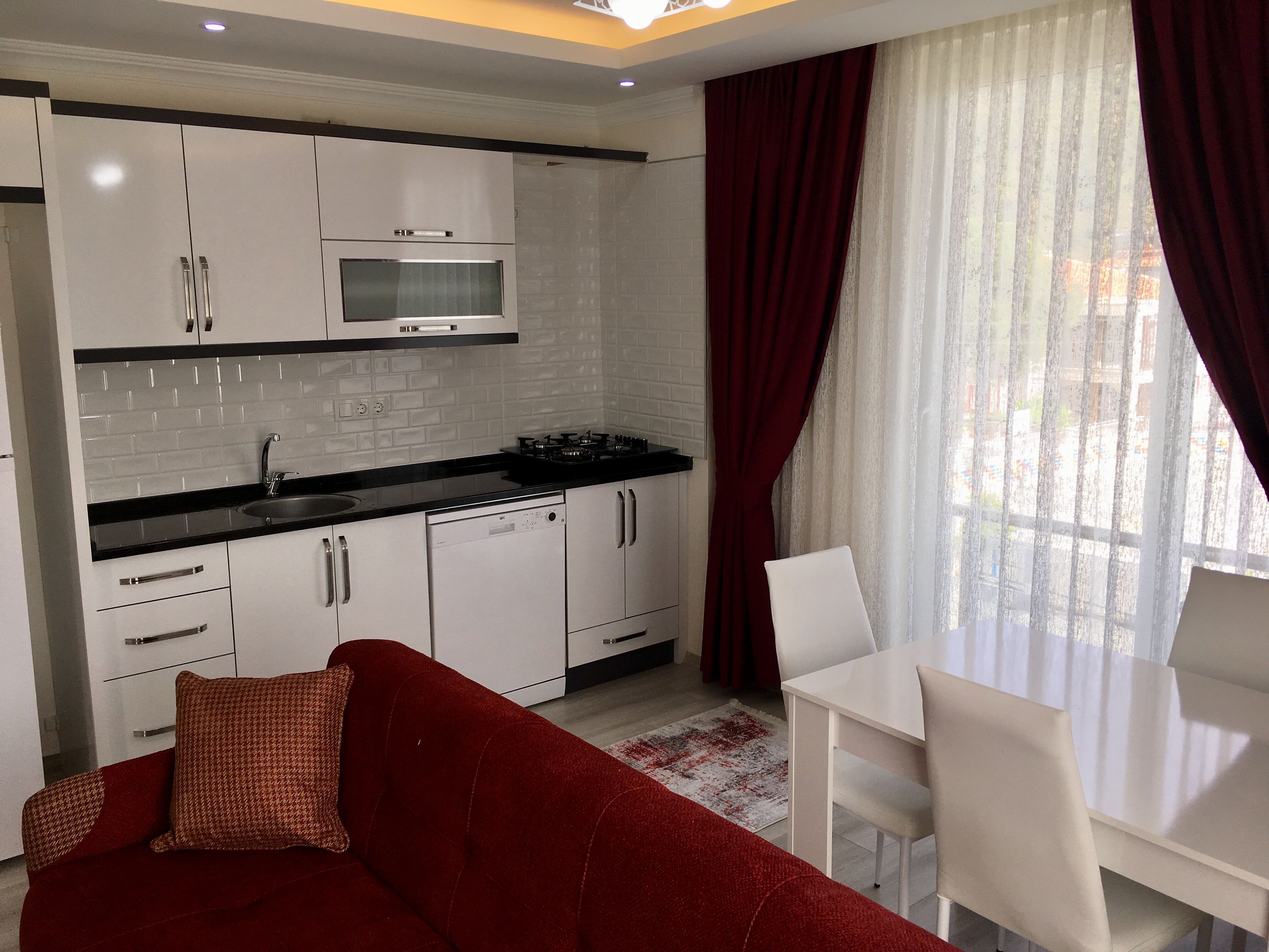 A modern kitchen with white cabinets, a microwave, and a dishwasher. There is a red sofa and a white dining table with chairs.