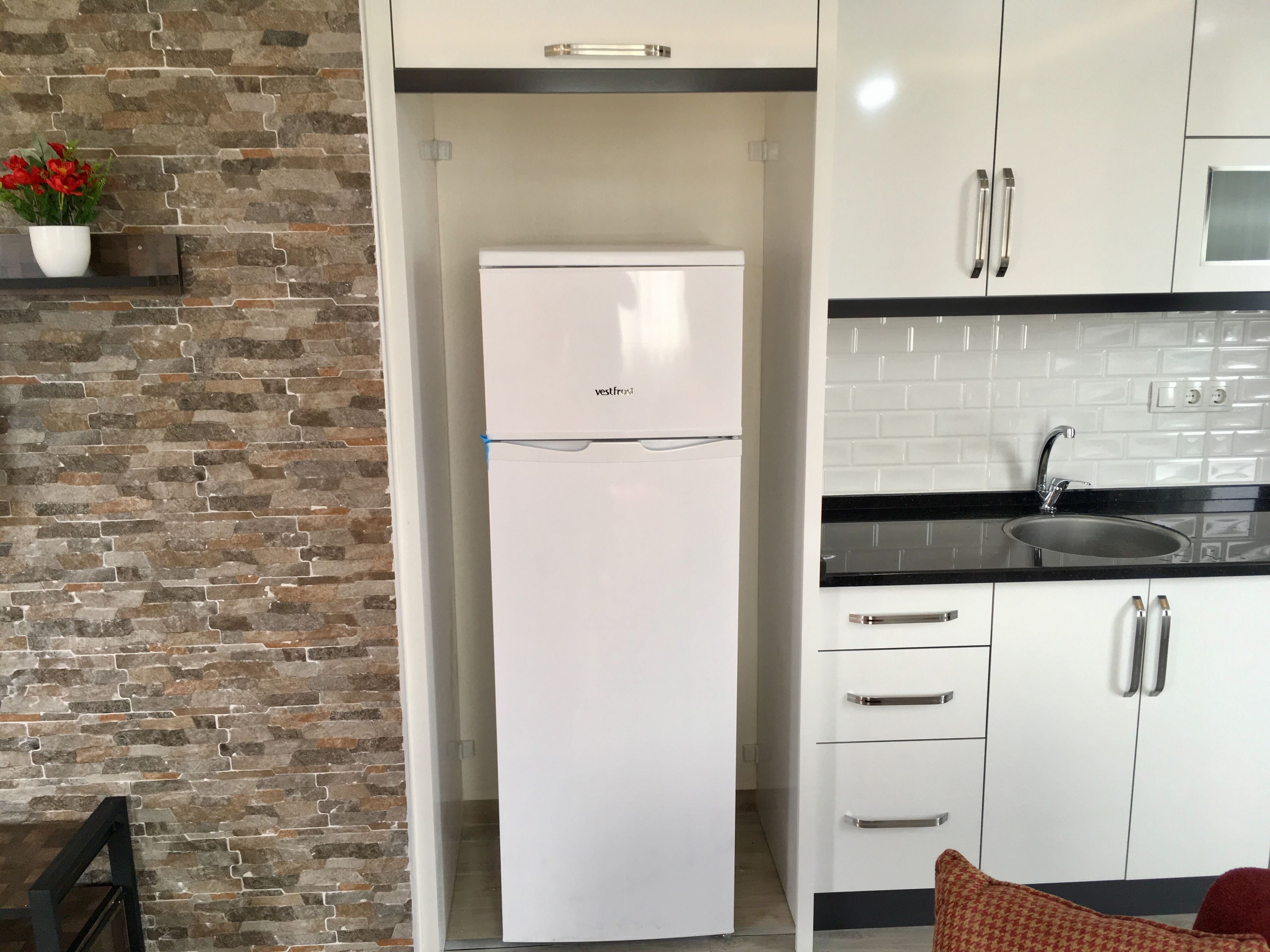 A compact kitchen with a white refrigerator, a black countertop, and a sink.