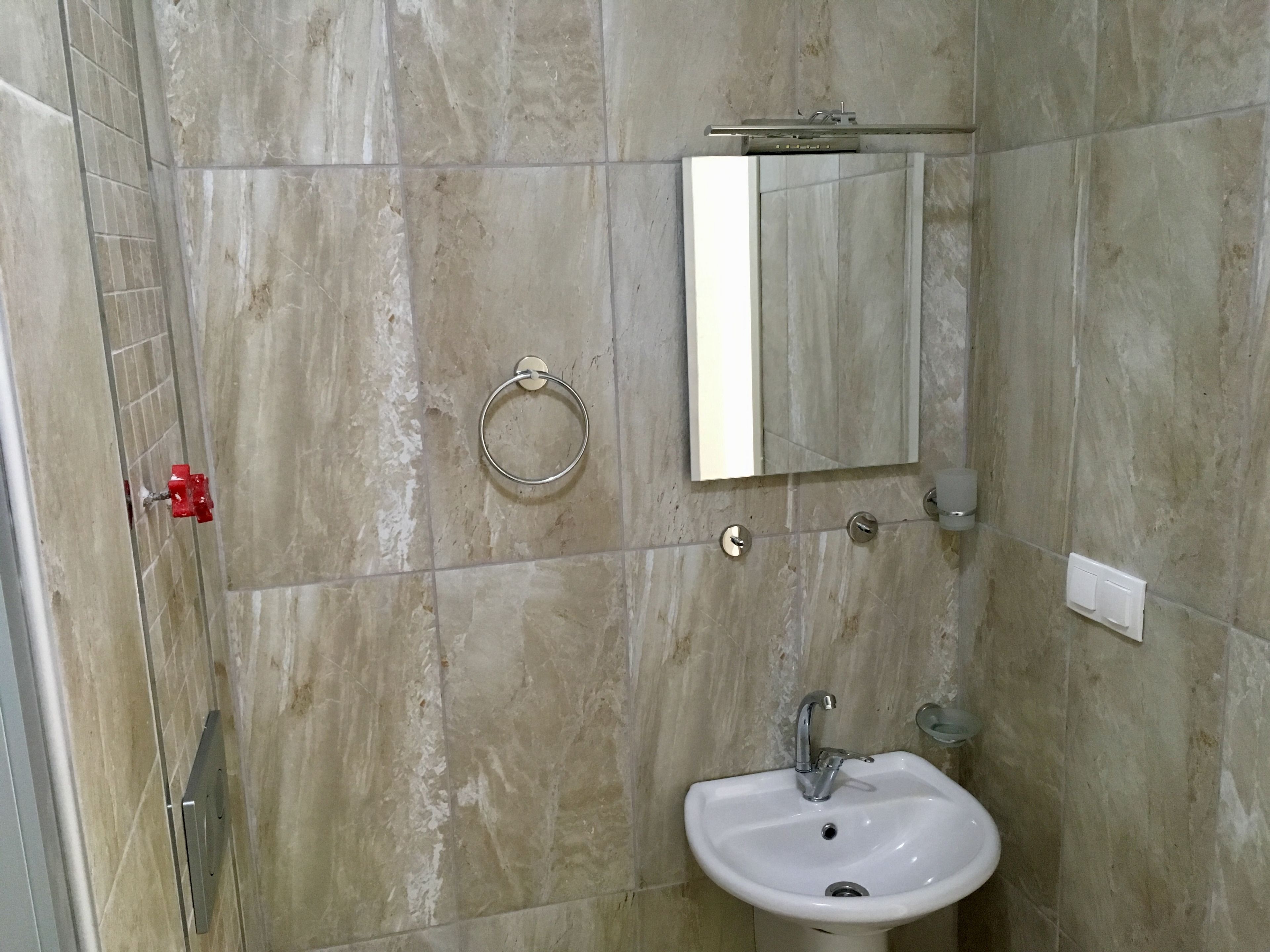 Une salle de bain avec un lavabo, un miroir, un porte-serviettes et une poignée de porte rouge.