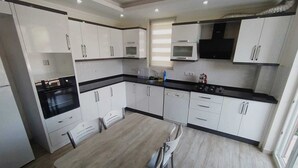 A modern kitchen with white cabinets, black countertops, and stainless steel appliances. - Kaya House Daily Flat (Ortaca)