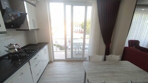 A modern kitchen with a gas stove, white cabinets, and a dining area with a table and chairs. - Kaya House Daily Flat (Ortaca)