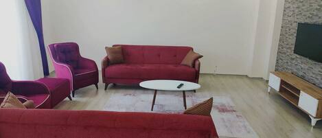 A living room with a red sofa, matching armchairs, a white coffee table, and a TV on a stone wall.