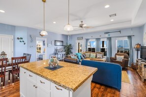 A spacious living area with a blue sofa, a dining table with chairs, and a kitchen island with granite countertop. - After Dune Delight 3 Bedroom Home by RedAwning (Port Bolivar)