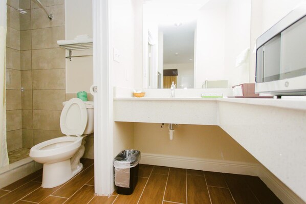 A bathroom with a toilet, shower, sink, and a television.