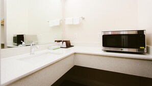 A modern bathroom with a white sink, a mirror, a microwave, and a towel rack.