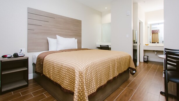 A modern hotel room with a wooden headboard, a large bed with a patterned bedspread, a bedside table with a phone, and a small shelf.