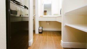 A narrow hallway with a refrigerator, a trash can, and a sink area with a mirror.