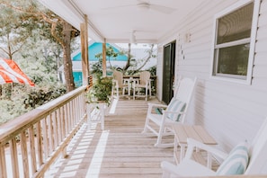 A covered porch with white wooden railings, a table, and two rocking chairs.