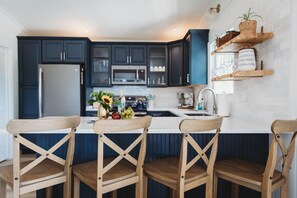 A modern kitchen with dark blue cabinets, a white countertop, and wooden chairs with a cross-back design.