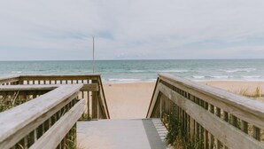 A wooden boardwalk leading to a beach with a clear view of the ocean. - ★ "The house is perfection—stylish, comfortable + close to the beach." (Nags Head)