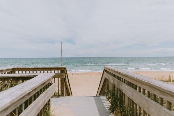 A wooden boardwalk leading to a beach with a clear view of the ocean.