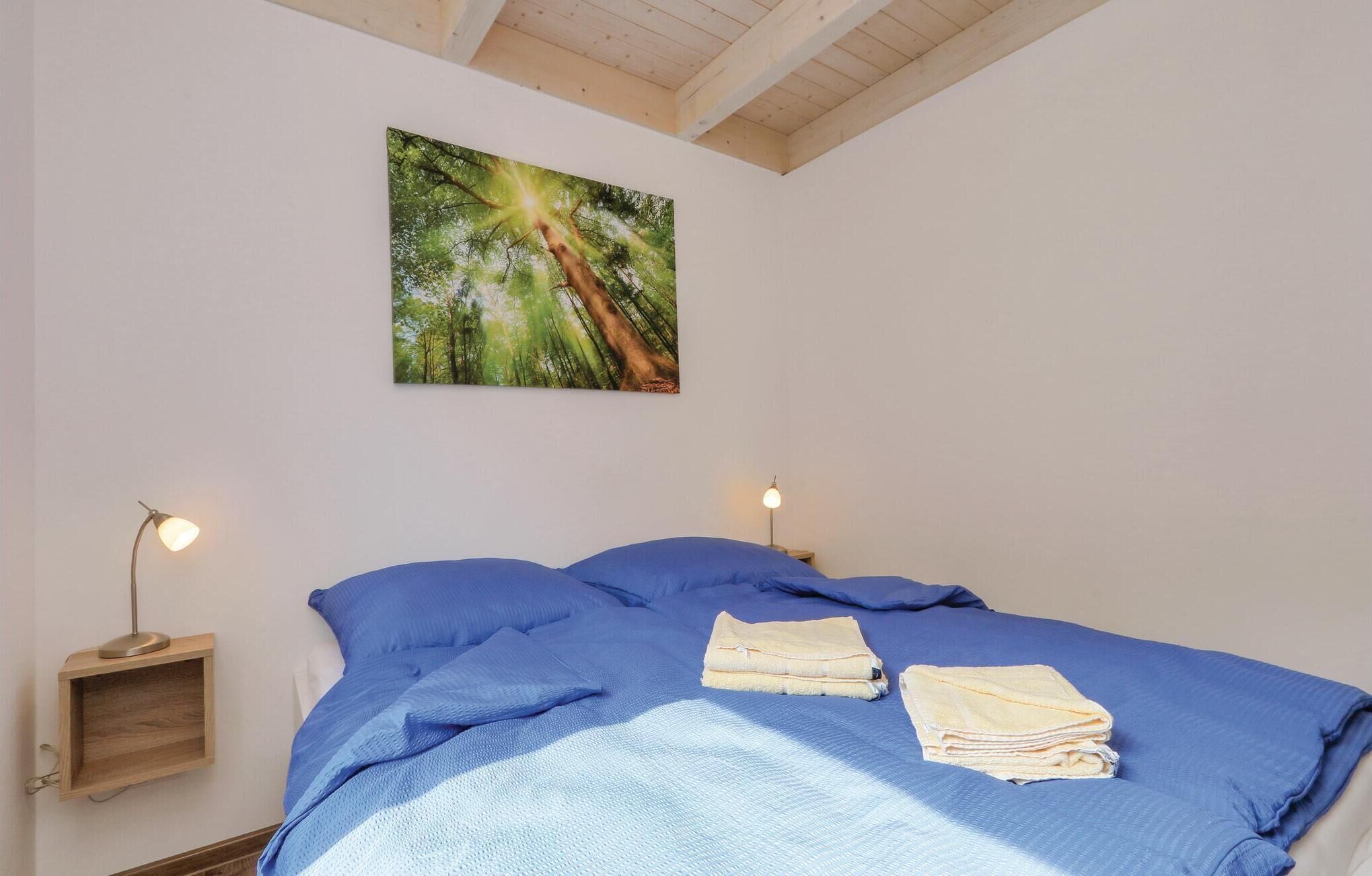 A bedroom with a bed, two bedside lamps, a wall-mounted painting, and a small wooden shelf.