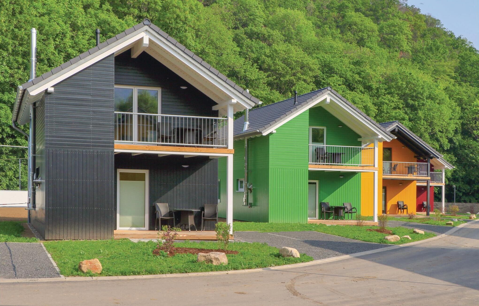 A row of colorful houses with balconies, set against a backdrop of lush green trees.