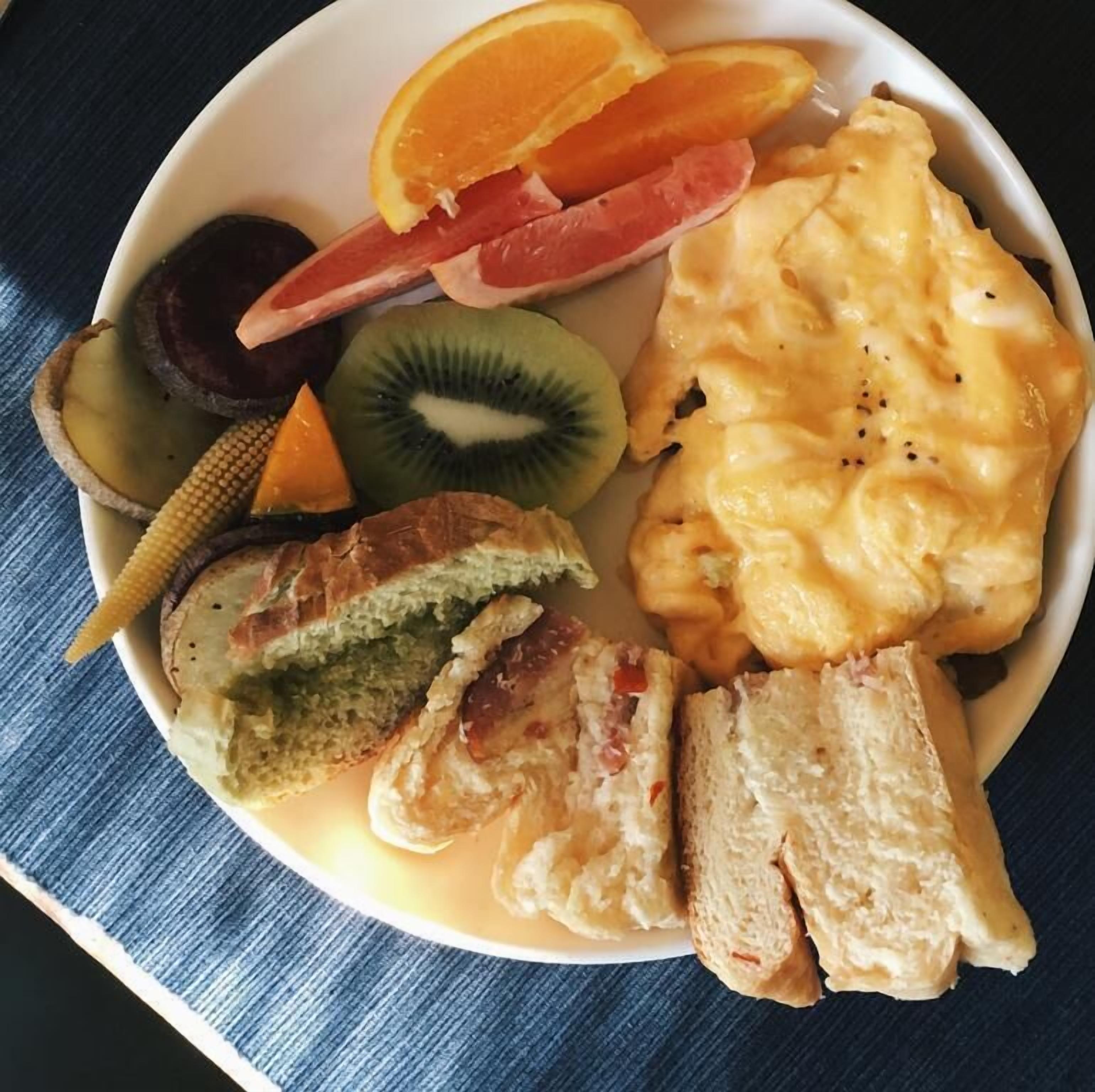 Un plato con huevos revueltos, tostadas, una rodaja de naranja, kiwi y un trozo de pan.