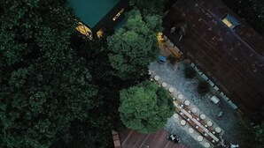 An aerial view of a property with a green-roofed building, a patio area with round tables, and a wooden deck. - Deep Breath B&B (Shoufeng)