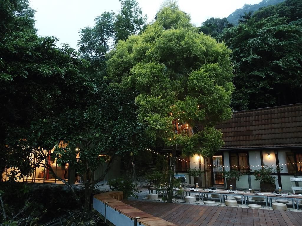 An outdoor seating area with wooden tables and chairs, surrounded by lush greenery and trees.
